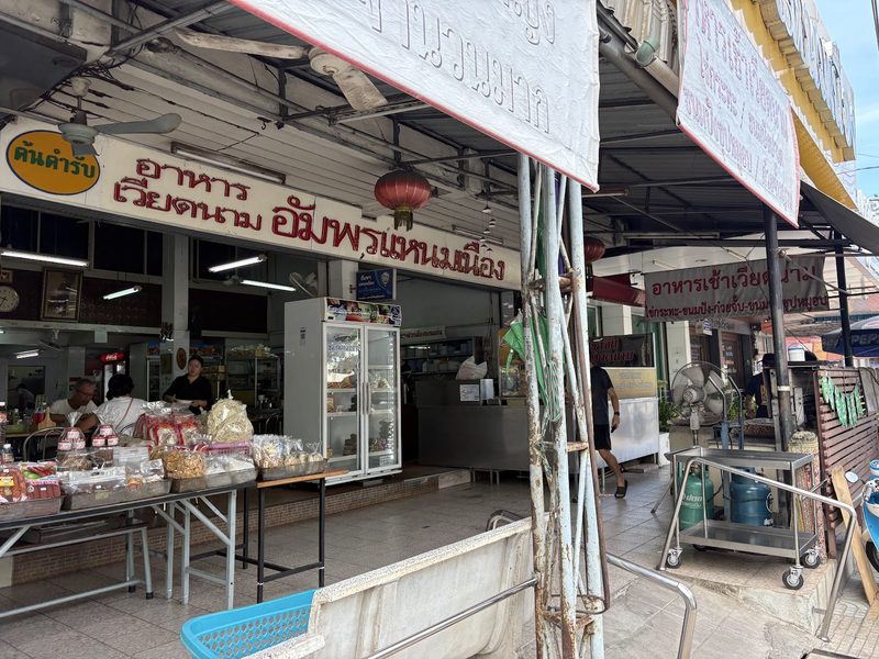 หน้าร้านอัมพรแหนมเนือง ป้ายตัวอักษรสีแดง อาหารเวียดนาม อัมพรแหนมเนือง กับป้ายต้นตำรับ และโต๊ะของฝากหน้าร้าน